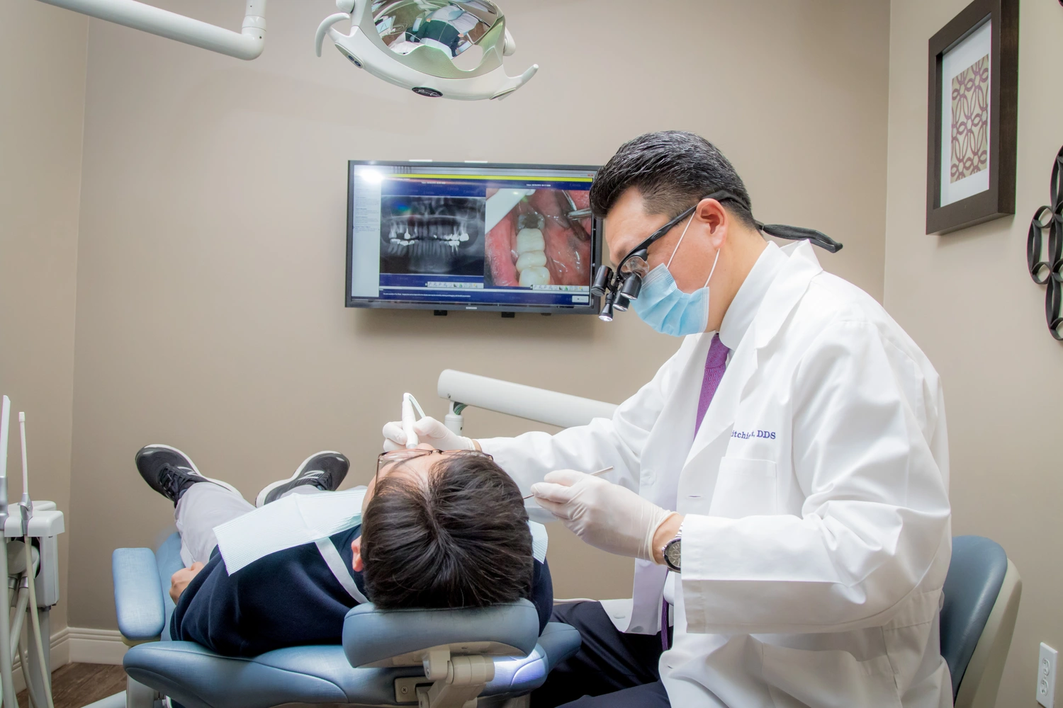 A man in a white coat is seated as a dentist conducts a dental examination.